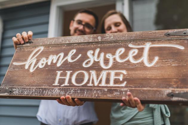 A couple holds a sign reading "Home Sweet Home"